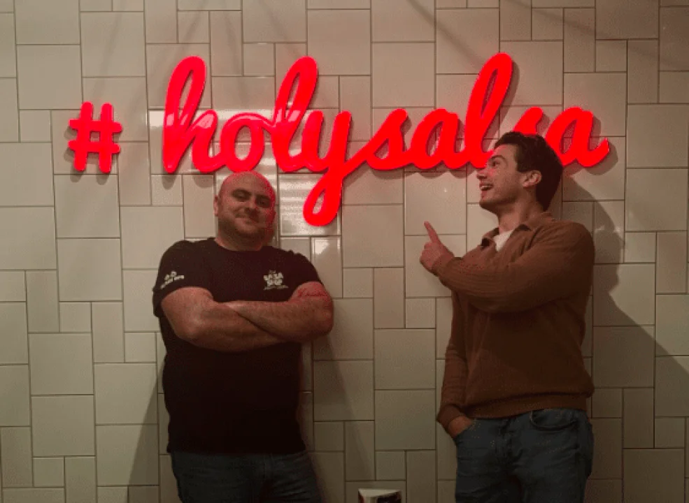 Our COO and friend from Mobietrain together pointing at a #holysalsa Salsa Shop logo on the wall.