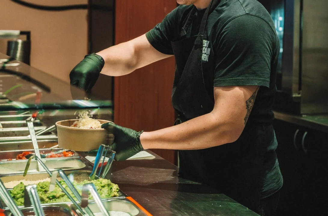 Salsa Shop employee preparing a fresh burrito bowl behind the counter, adding ingredients like rice, beans and toppings during the build-your-own ordering process.