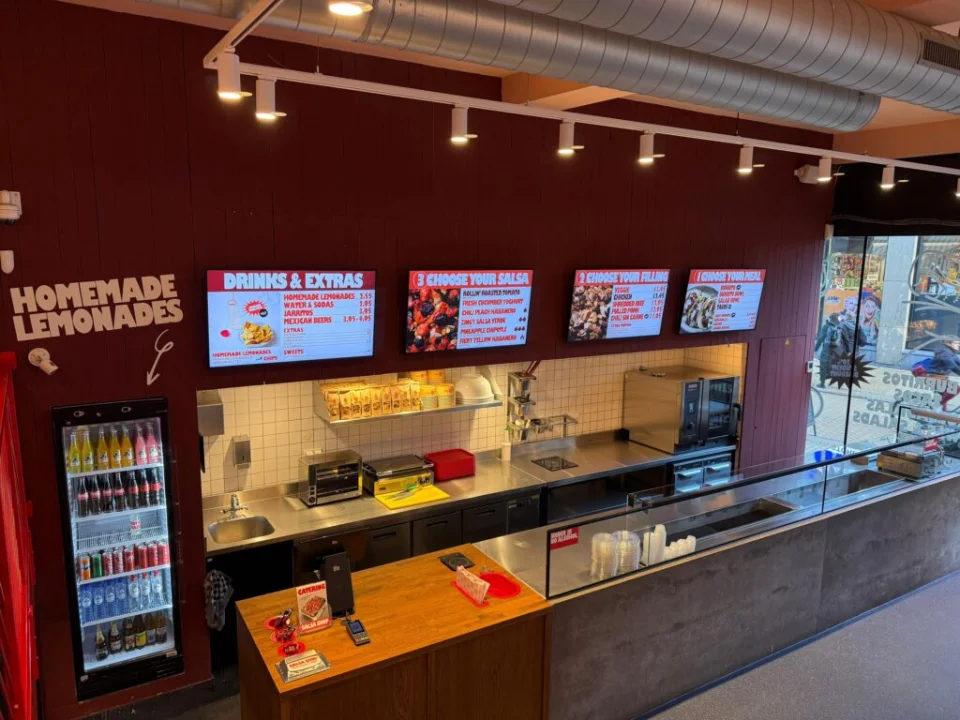Interior of a Salsa Shop restaurant showing the service counter and ordering line with digital menu boards displaying burritos, bowls and fresh Mexican ingredients.