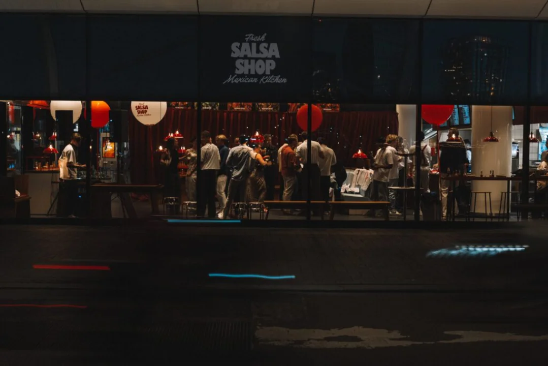 View from outside the Salsa Shop at Amsterdam Central, showing people inside celebrating with food, drinks, and music during the anniversary event.